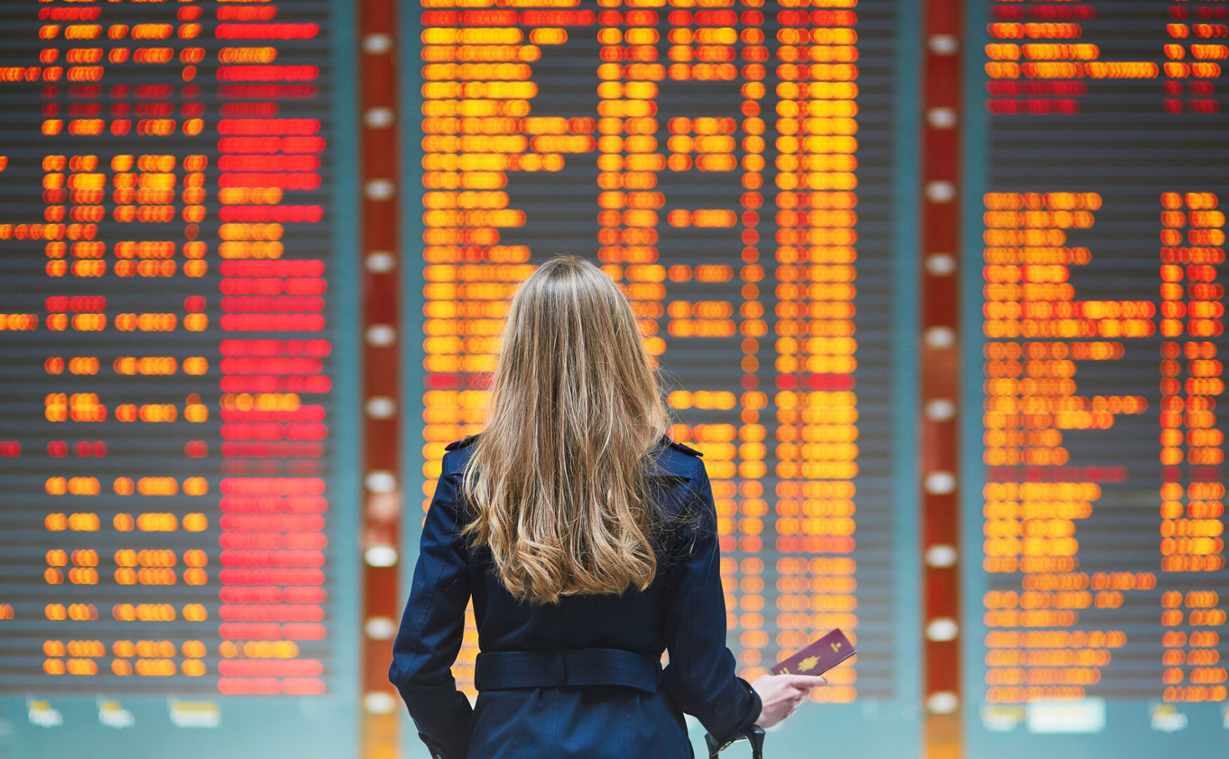 Woman traveler in front of airport departures board also known as a FID, Flight Information Display.